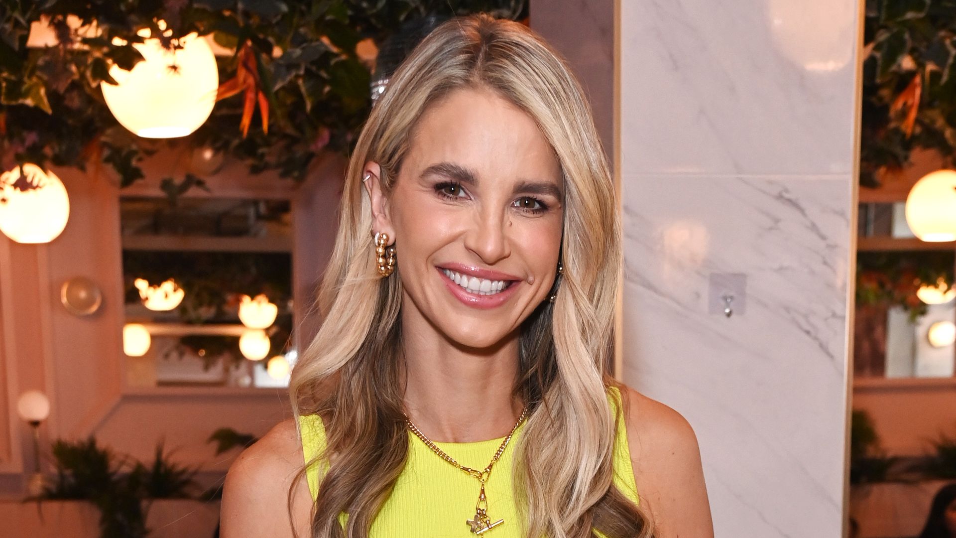 Vogue Williams in a yellow top and blue jeans standing in a restaurant area while at an event