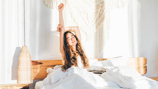 Woman relaxing on a bed. Woman stretching hands in bed.