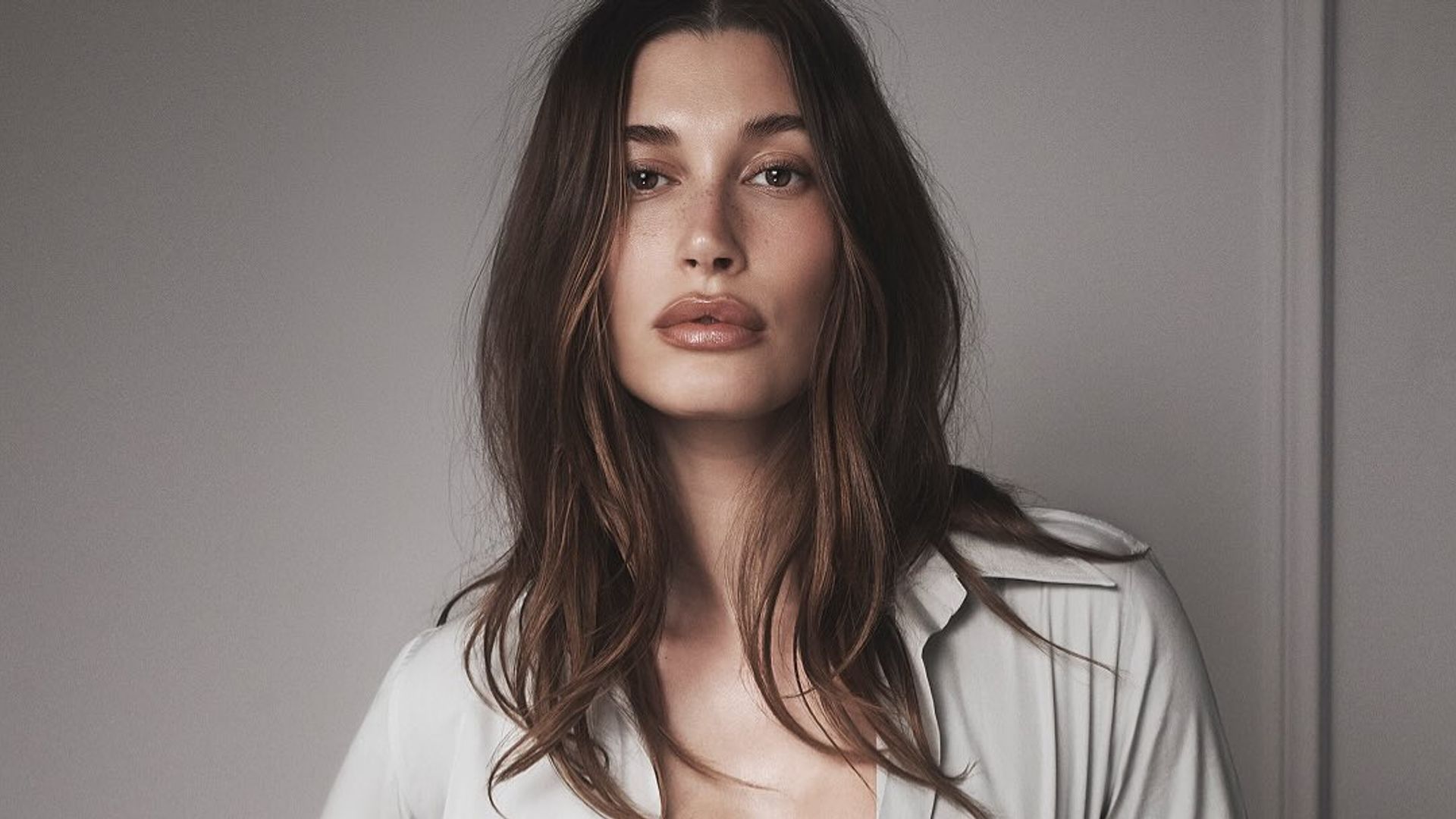 Hailey Bieber poses in a grey shirt for Rhode