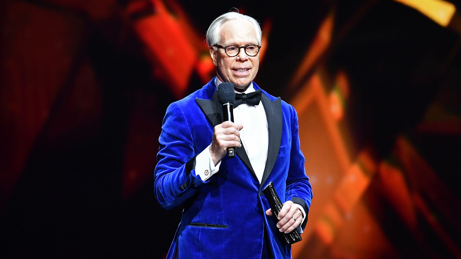 Tommy Hilfiger stood on stage smiling with a mic in hand