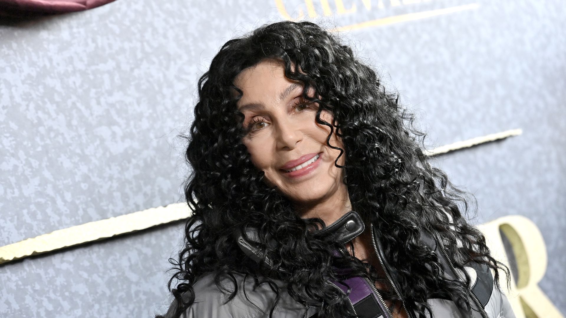 Cher shows off her curly black hair and wears a puffer jacket