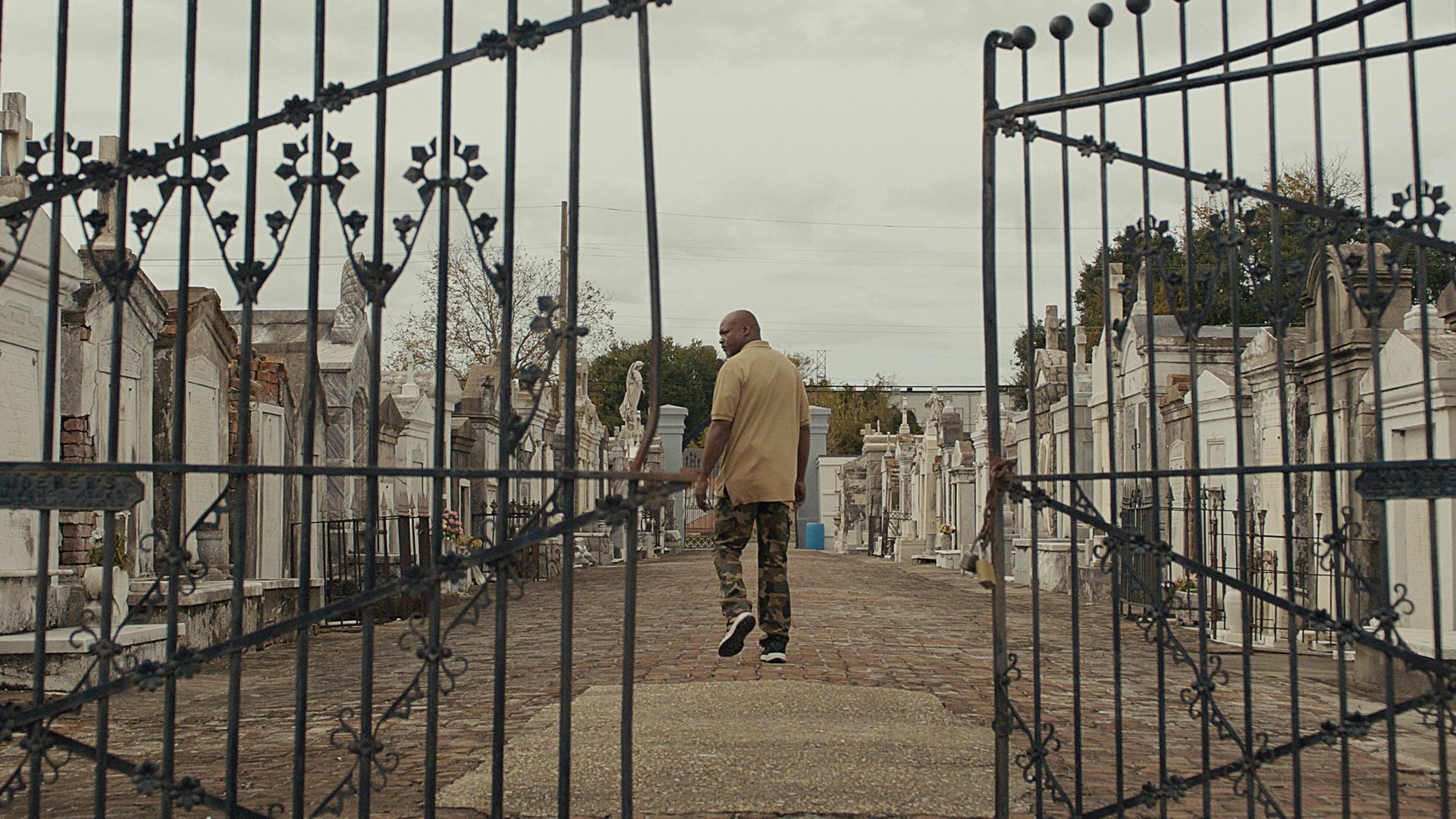 A Black man walking into a graveyard with mausoleums