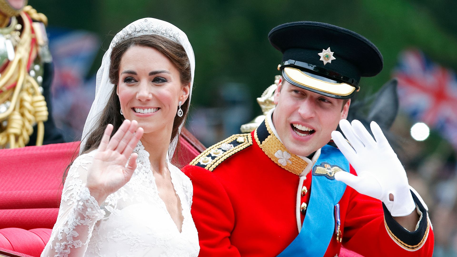 Catherine in bridal gown waving and Prince William (wearing his red tunic uniform of the Irish Guards, of which he is Colonel) travel down The Mall