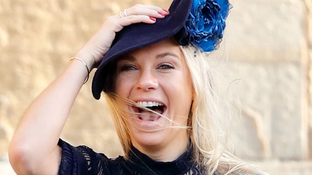 Chelsy Davy in blue dress laughing as she holds her hat at the wedding of Princess Eugenie of York and Jack Brooksbank
