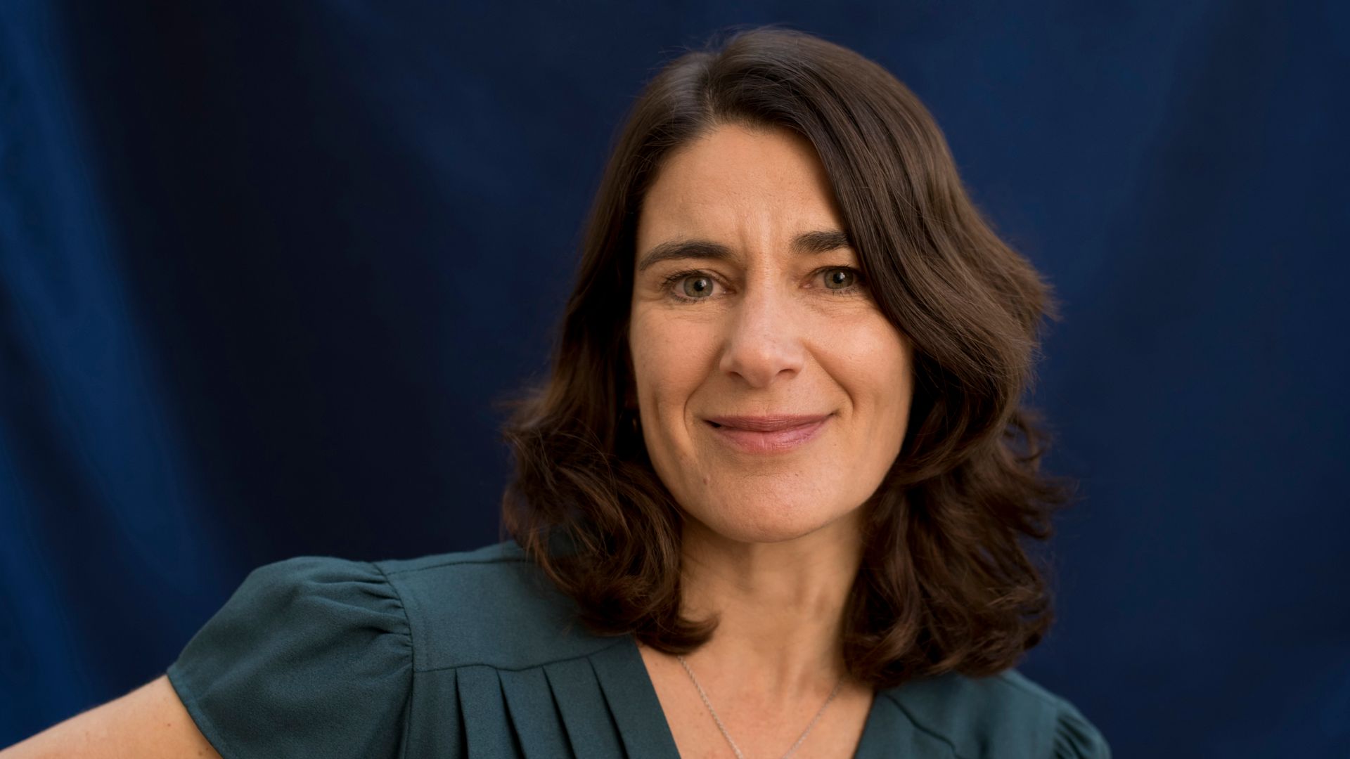 Woman smiling against a dark background in a teal top