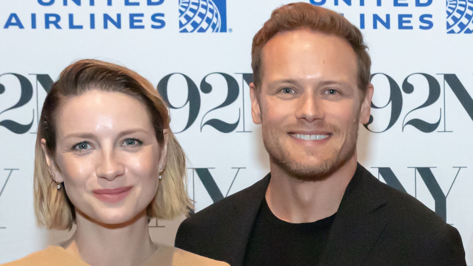 Sam Heughan and Caitriona Balfe smiling on a red carpet