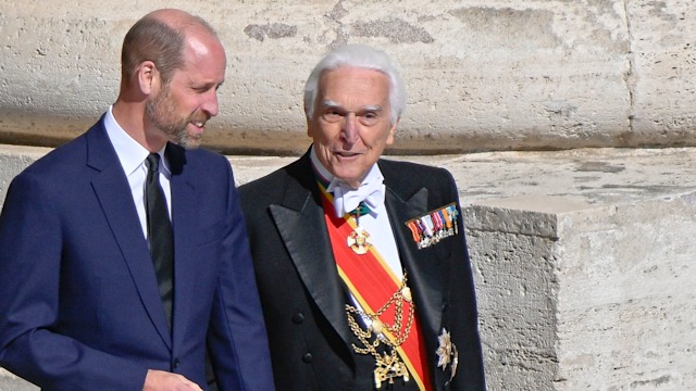 Prince William in a blue suit walking alongside a man in a black suit