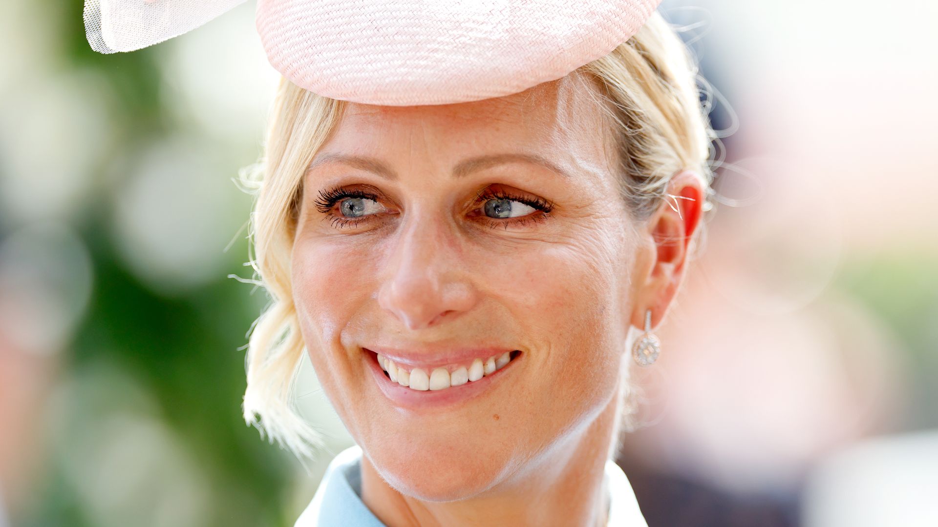  Zara Tindall smiling shoulders up in blue dress and pink hat