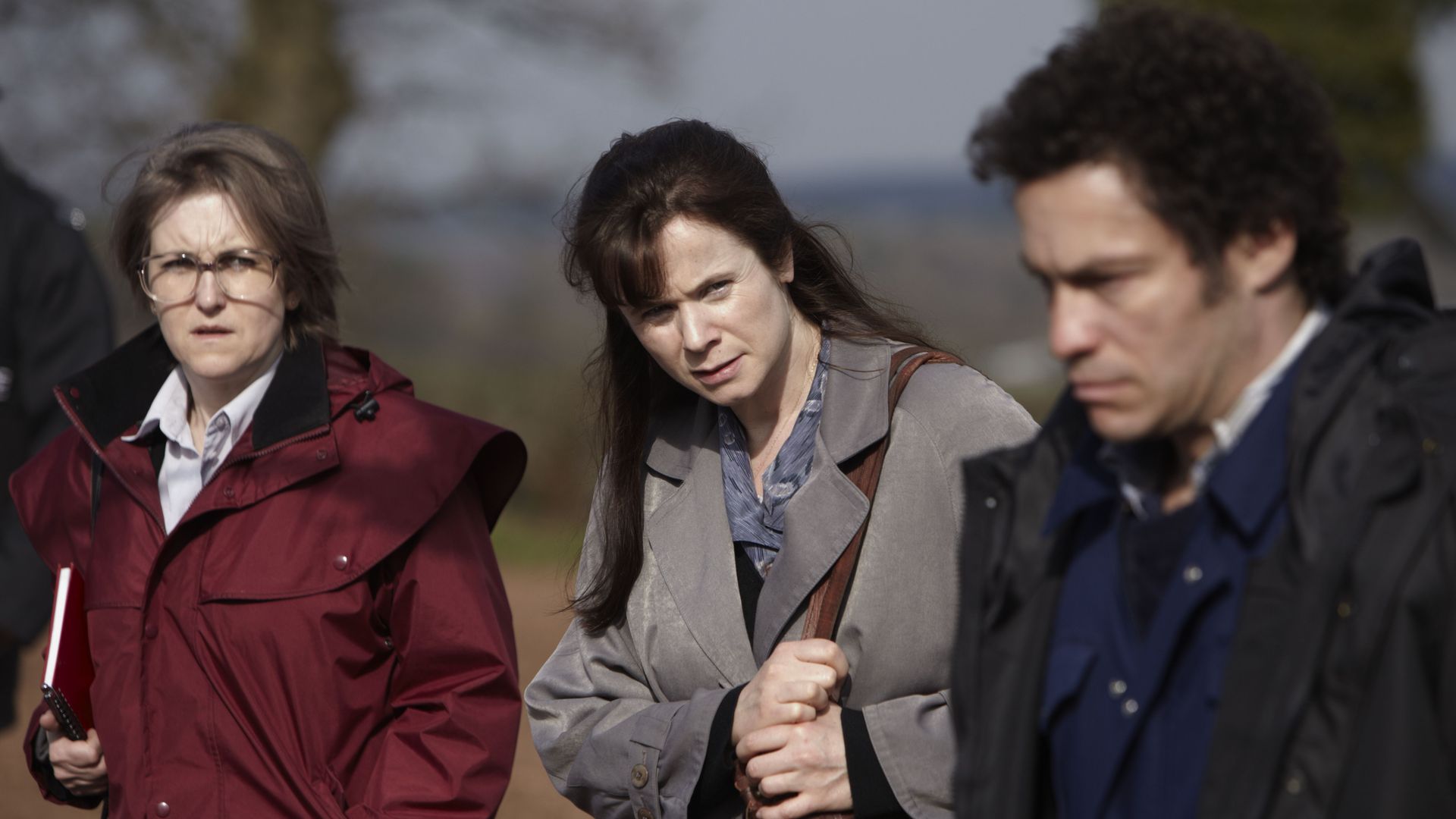 two women and a man in coats walking in field