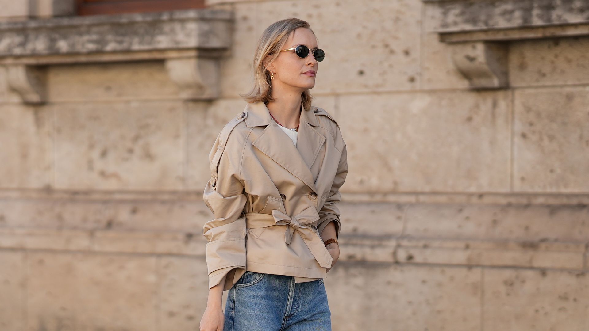 Marlies Pia Pfeifhofer is seen wearing a cropped beige double-breasted trench jacket with waist belt, wide lapels, raglan sleeves and shoulder epaulettes from Pennyblack; a cream white sleeveless textured linen top with round neckline and asymmetric front panel from Sezane; light blue washed ultra wide leg Paloma jeans in structured denim with high waist and long flared silhouette from Citizens of Humanity; beige Dolly Verona raffia platform sandals with thick sole from LarroudÃ©; a pastel matcha green Fendi Mamma Baguette  Small shoulder bag in soft nappa leather with top handle, flap closure and FF logo buckle in golden metal hardware; oval sunglasses with black lenses and golden temples from Persol; a surigao pearl necklace with red Japanese glass beads and a freshwater baroque pearl from Les Beads Studio; golden Nature hoop earrings from Ole Lynggaard; a golden Leaves ring large from Ole Lynggaard; a vintage light brown leather Tank wristwatch from Cartier; her blonde hair is worn in a side-parted bob on July 18, 2025 in Munich, Germany