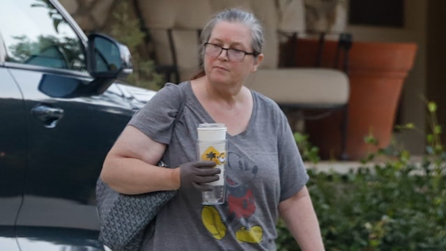 Bridget Fonda walking with coffee cup in gray shirt