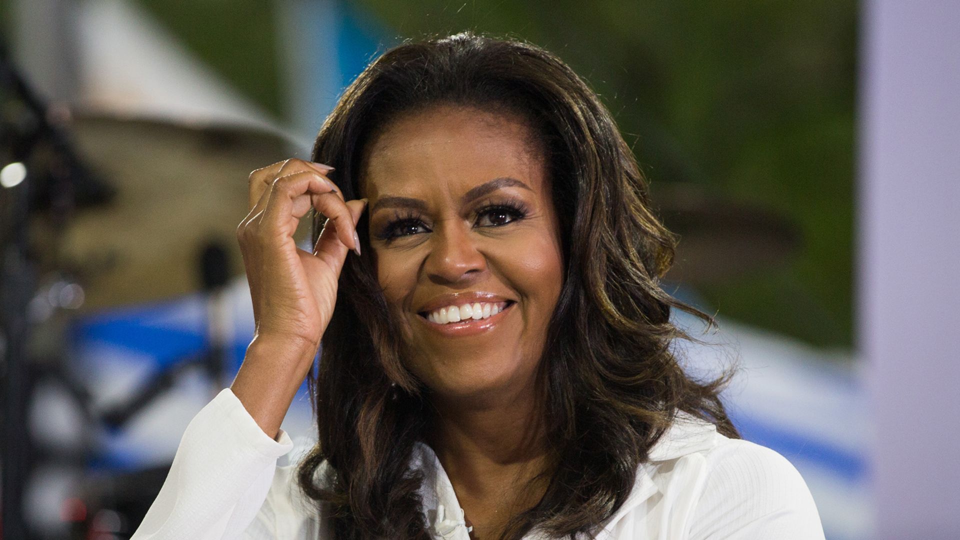 Michelle Obama smiles while wearing a white suit