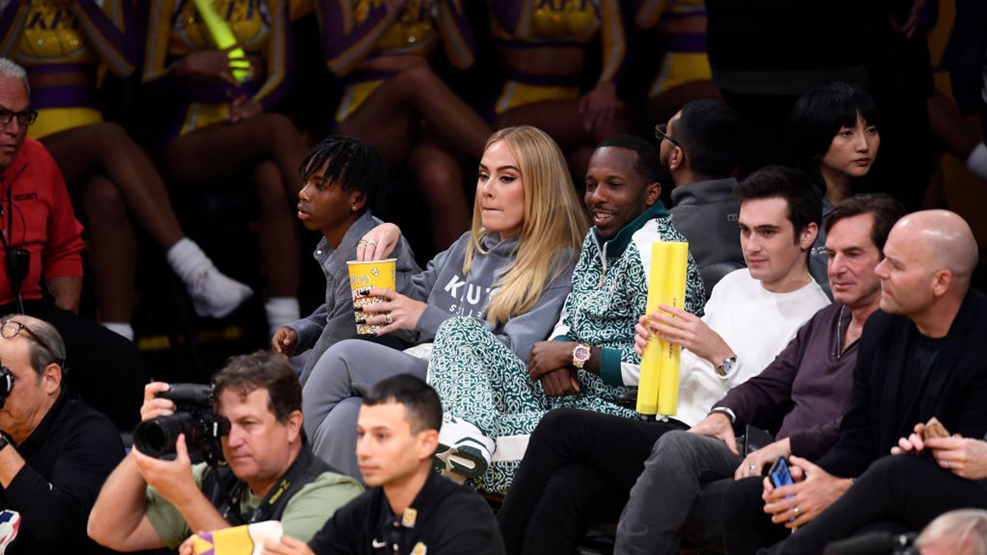 Adele in a grey hoodie and pants from Rich's brand Klutch Athletics Apparel as she watches the basketball game with him