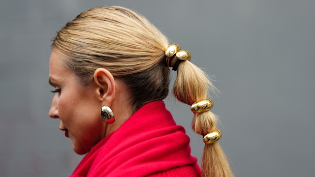 A guest wears a red scarf, red wool top, golden jewelry as attachments for the ponytail, earrings, outside Brandon Maxwell, 