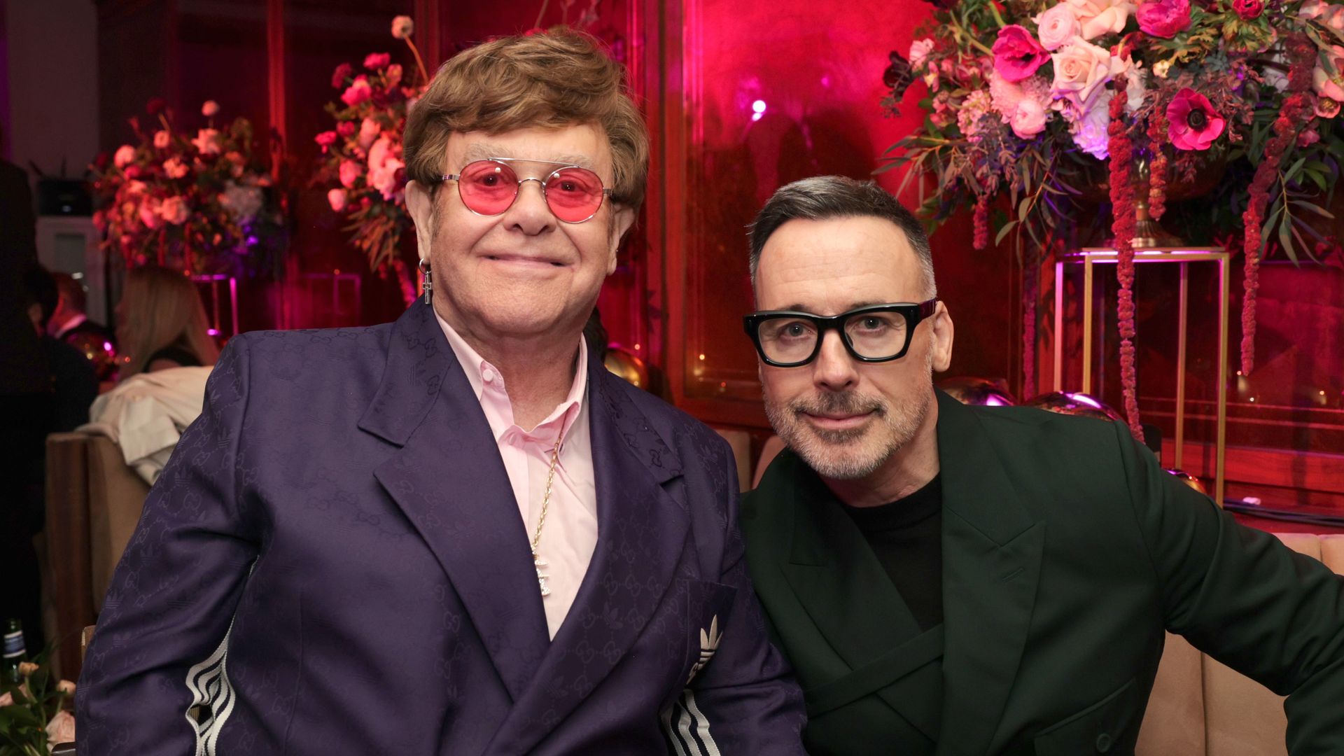 Elton John and David Furnish sit on couch at Oscars Party