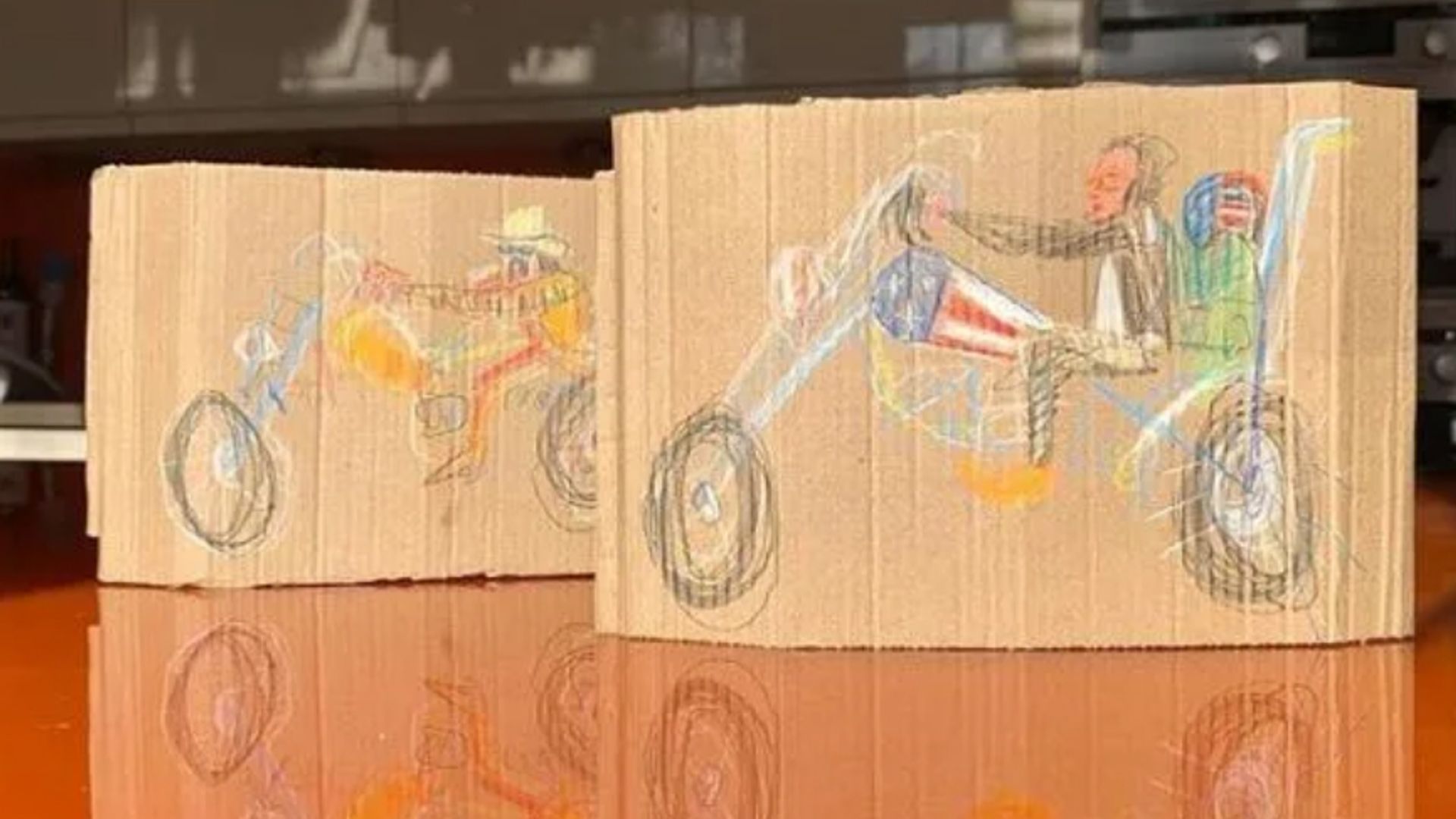 Two drawings on cardboard of people riding motorcycles