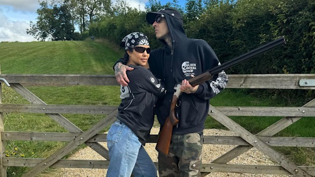 Kourtney Kardashian and Travis Barker posing with a labrador and a gun 