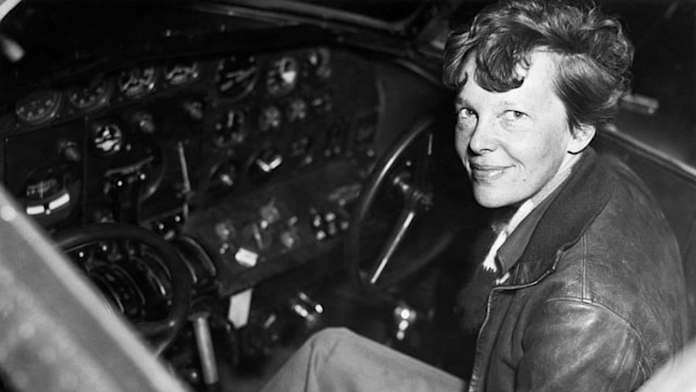Amelia Earhart smiles as she sits clad in a leather aviator's jacket in the cockpit of a small airplane, 1937