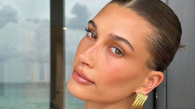 Hailey Bieber poses for a photo in a gold dress and matching earrings