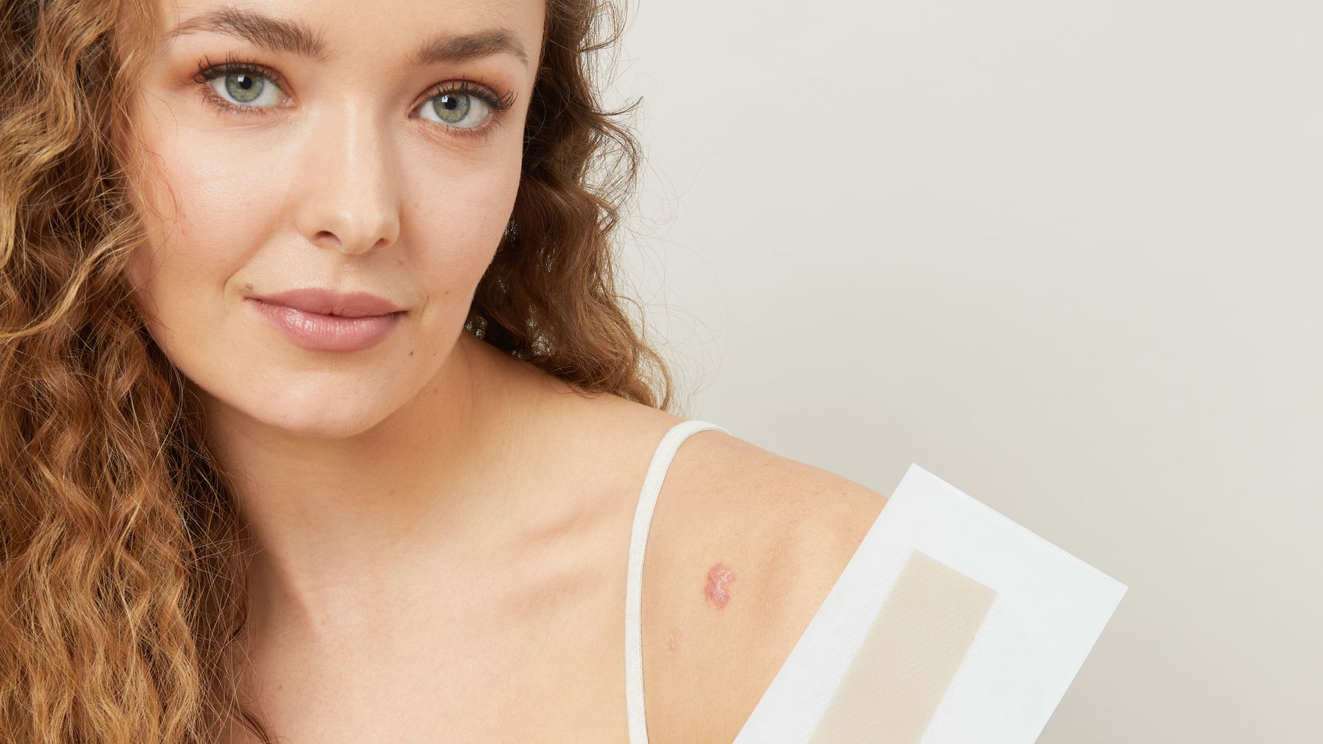 Woman holding Scar Erase silicone strip, she has a scar on her right shoulder