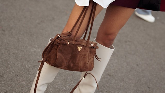 A guest wears white shirt, burgundy jacket, burgundy coat, brown Prada bag and white long boots during the 10th season of the Visa Fashion Week Almaty on October 18, 2024 in Almaty, Kazakhstan. (Photo by Raimonda Kulikauskiene/Getty Images)