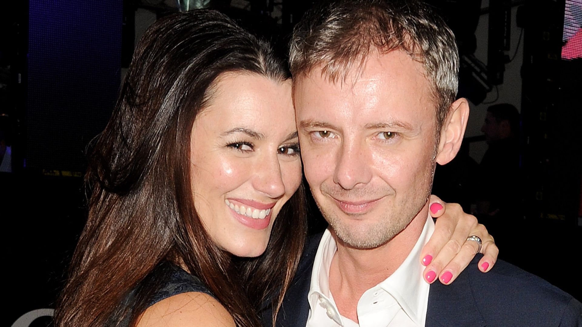 John Simm in a blue suit and white shirt hugging his wife Kate in a dress