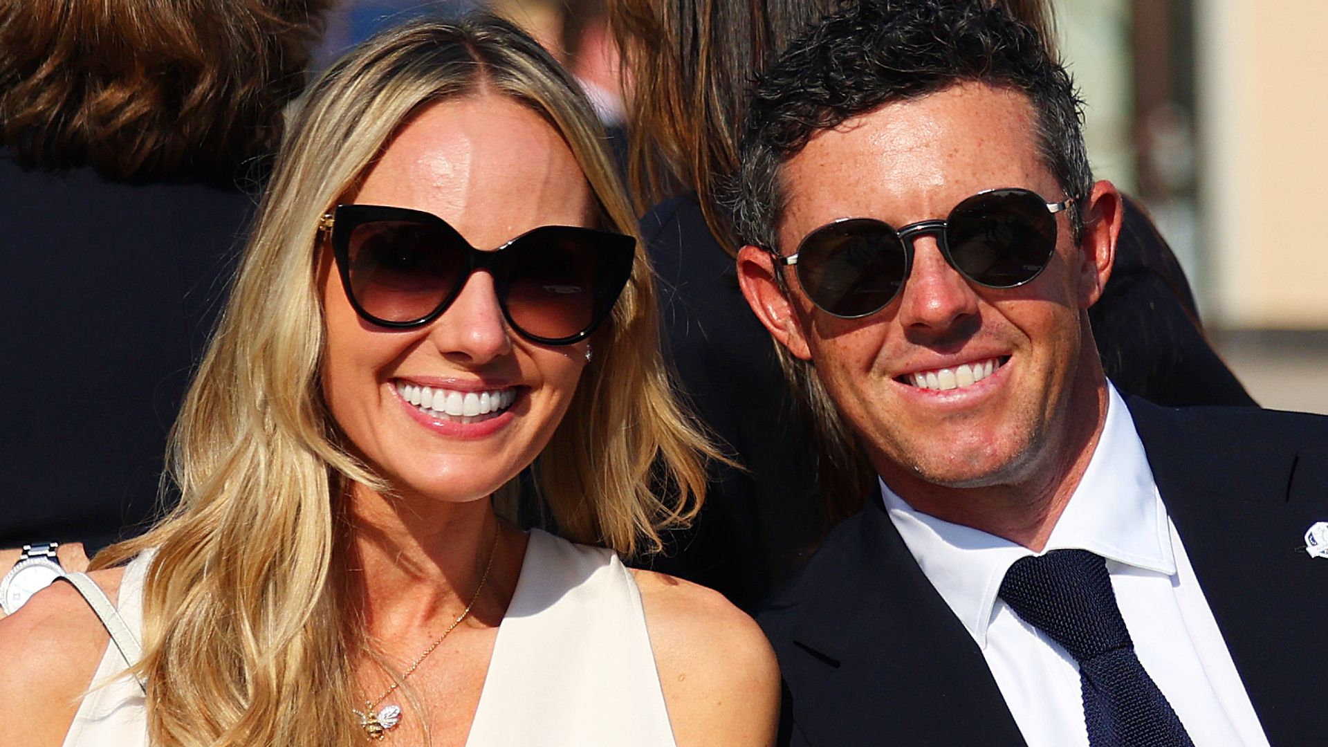 Rory McIloroy in a suit and sunglasses with his wife Erica in a white dress