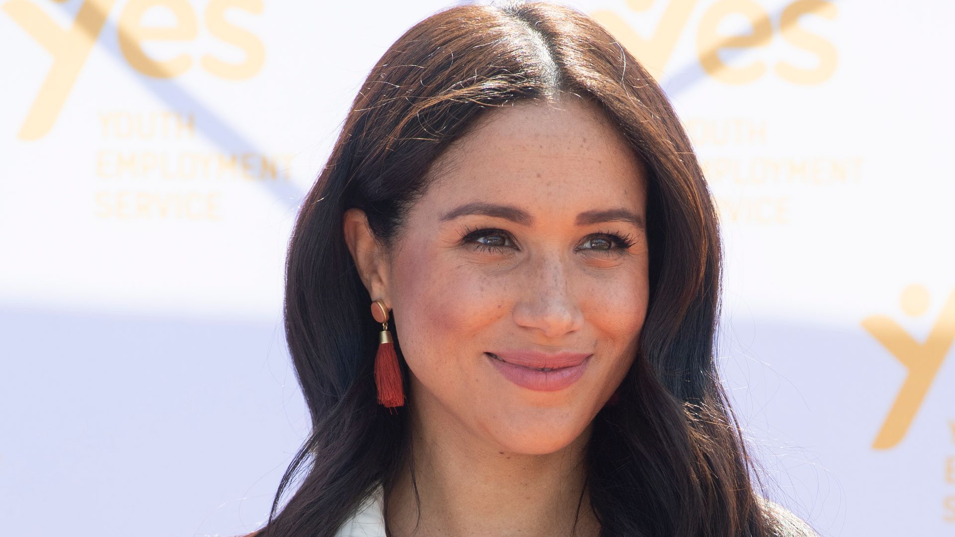 Meghan, Duchess of Sussex in white shirt dress with hands clasped