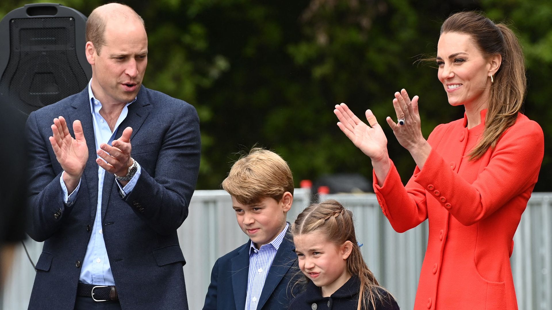 Prince William in suit and Catherine in red coat with george and charlotte clapping