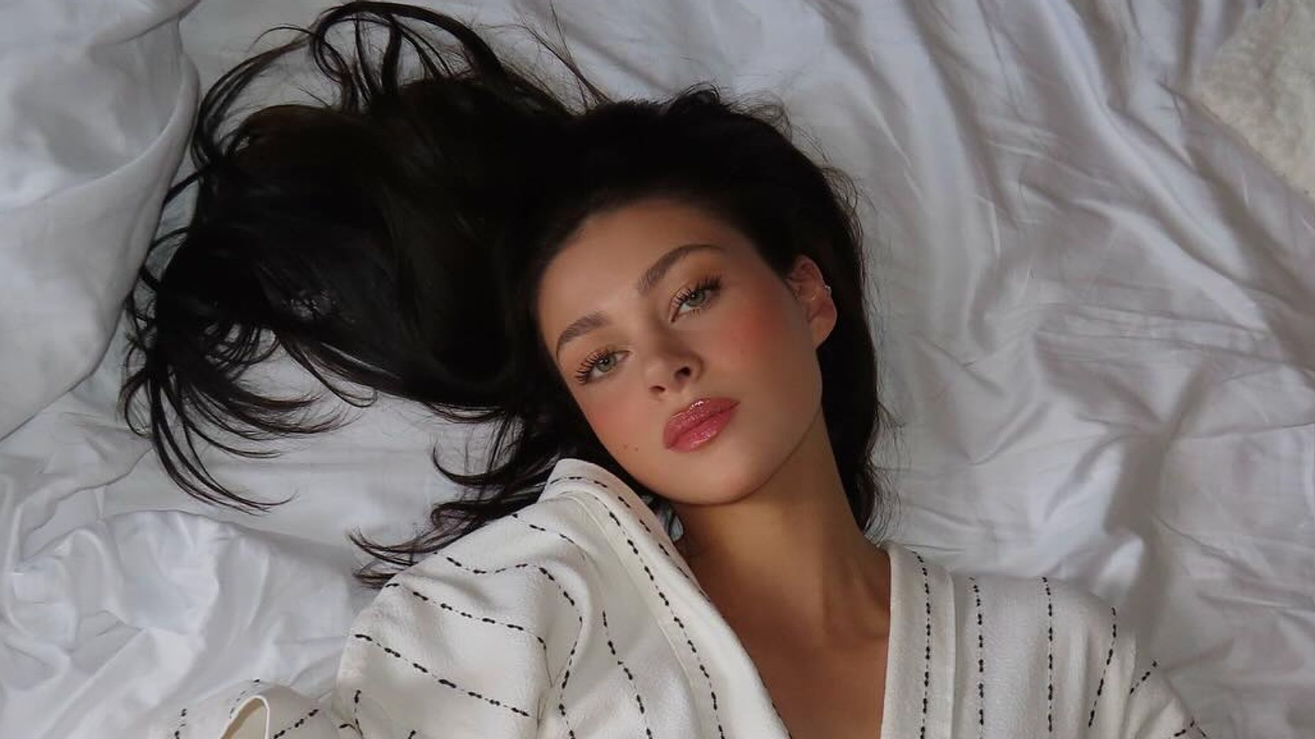 Nicola Peltz Beckham poses in a robe on a bed