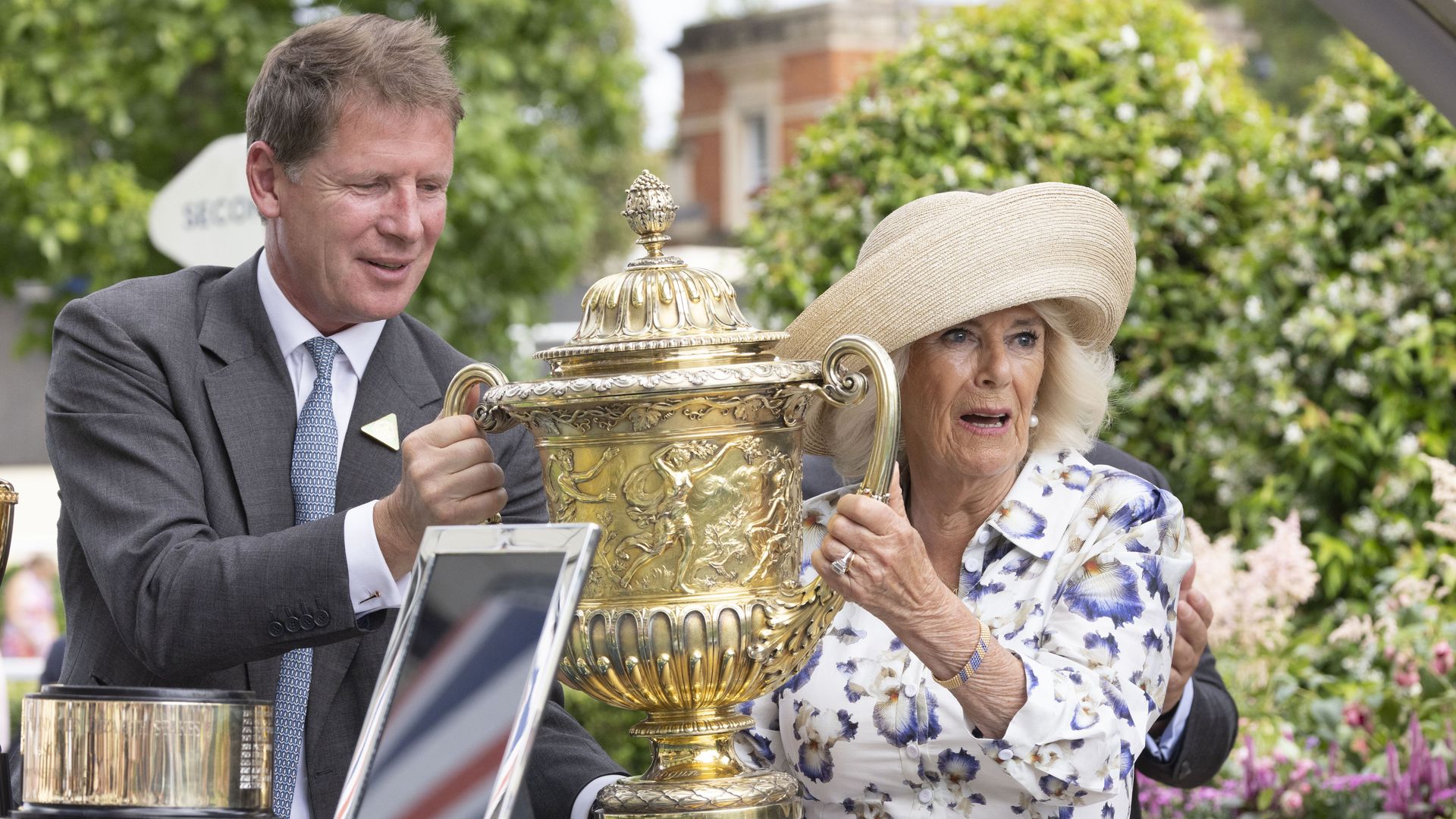 Queen Camilla and a man carrying a golden trophy