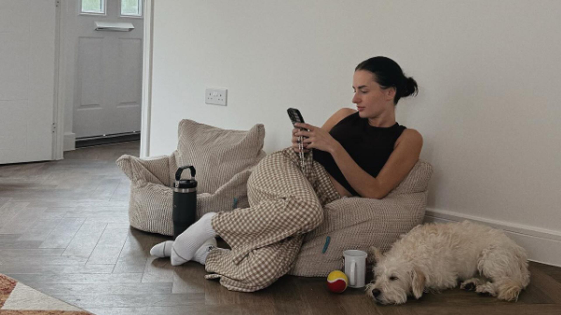 Amber Davies sitting in a tiny armchair in an unfurnished room with a dog