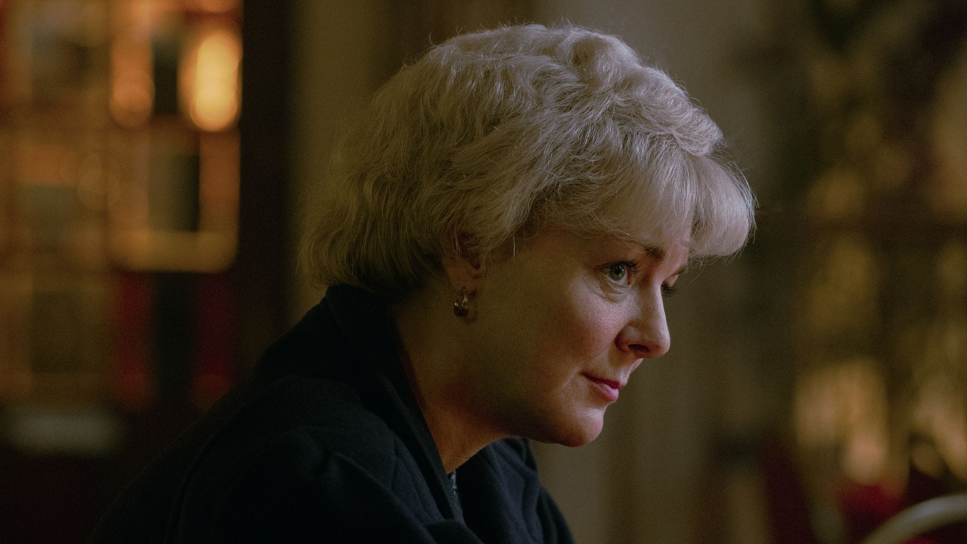 A blonde woman sits with her hands clasped