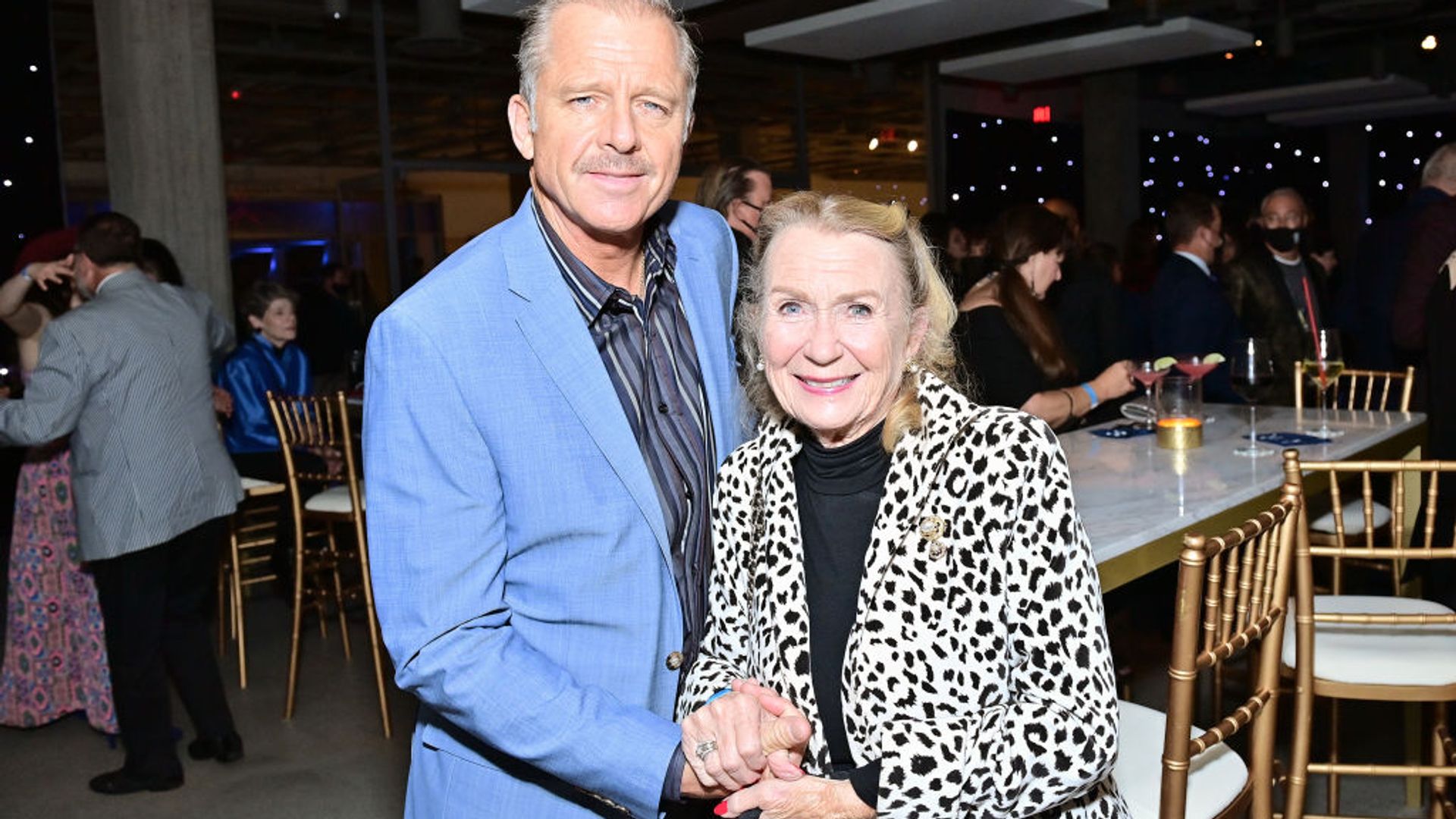 Juliet Mills wearing a leopard print blazer and Maxwell Caulfield wearing a blue blazer and navy striped shirt at a TCM event in 2022. 