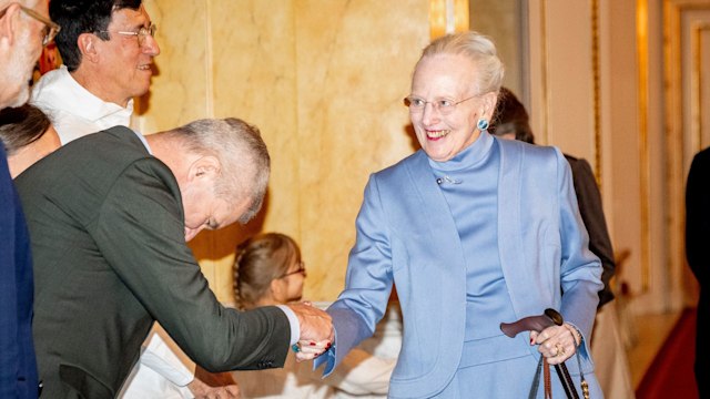 Queen Margrethe in a blue dress shaking hands with a bowing man