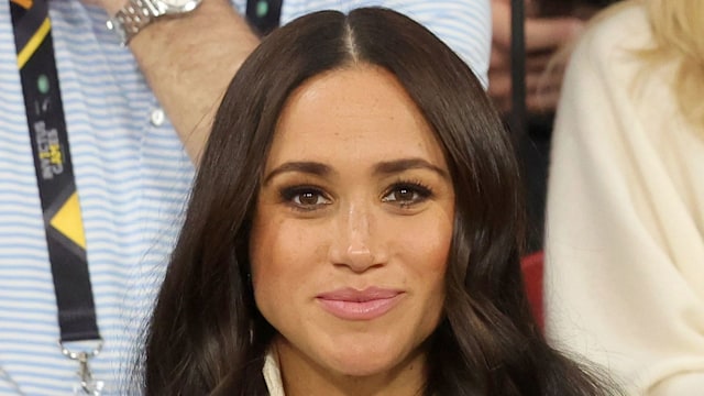 Meghan Markle in a tan coat with a blank expression
