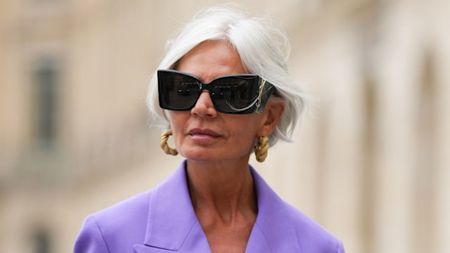 Grece Ghanem wears black sunglasses from Saint Laurent, a beige leather and gold braided earrings, a purple oversized blazer jacket, matching purple large suit pants, a dark brown shiny braided leather handbag,  outside the COS show, on April 26, 2023 in Paris, France. 