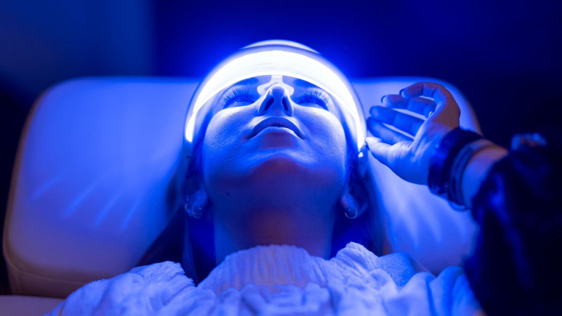 Woman using blue LED light therapy mask at home
