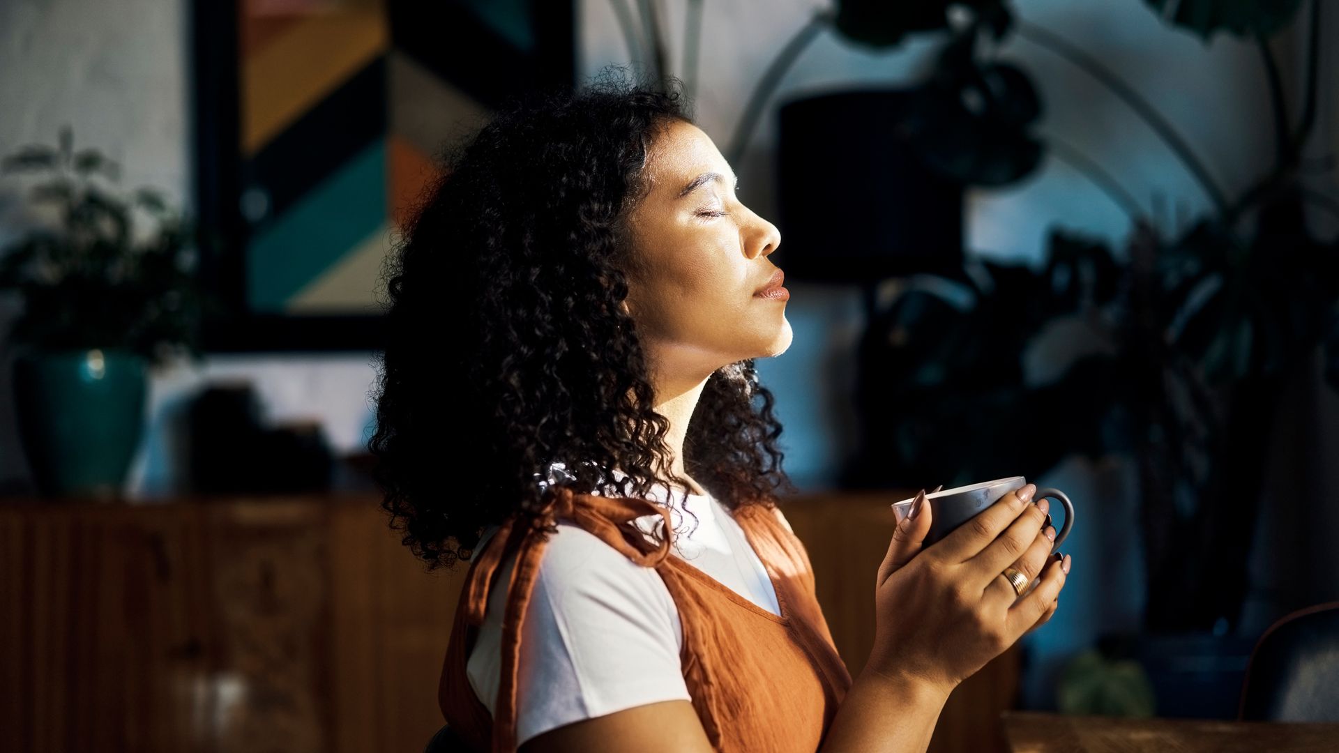 A woman drinking coffee and meditating in her home with her eyes closed. 