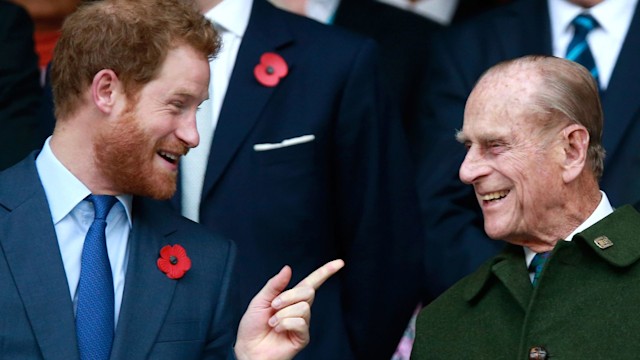 Prince Harry pointing and smiling at Prince Phillip dressed in a green coat