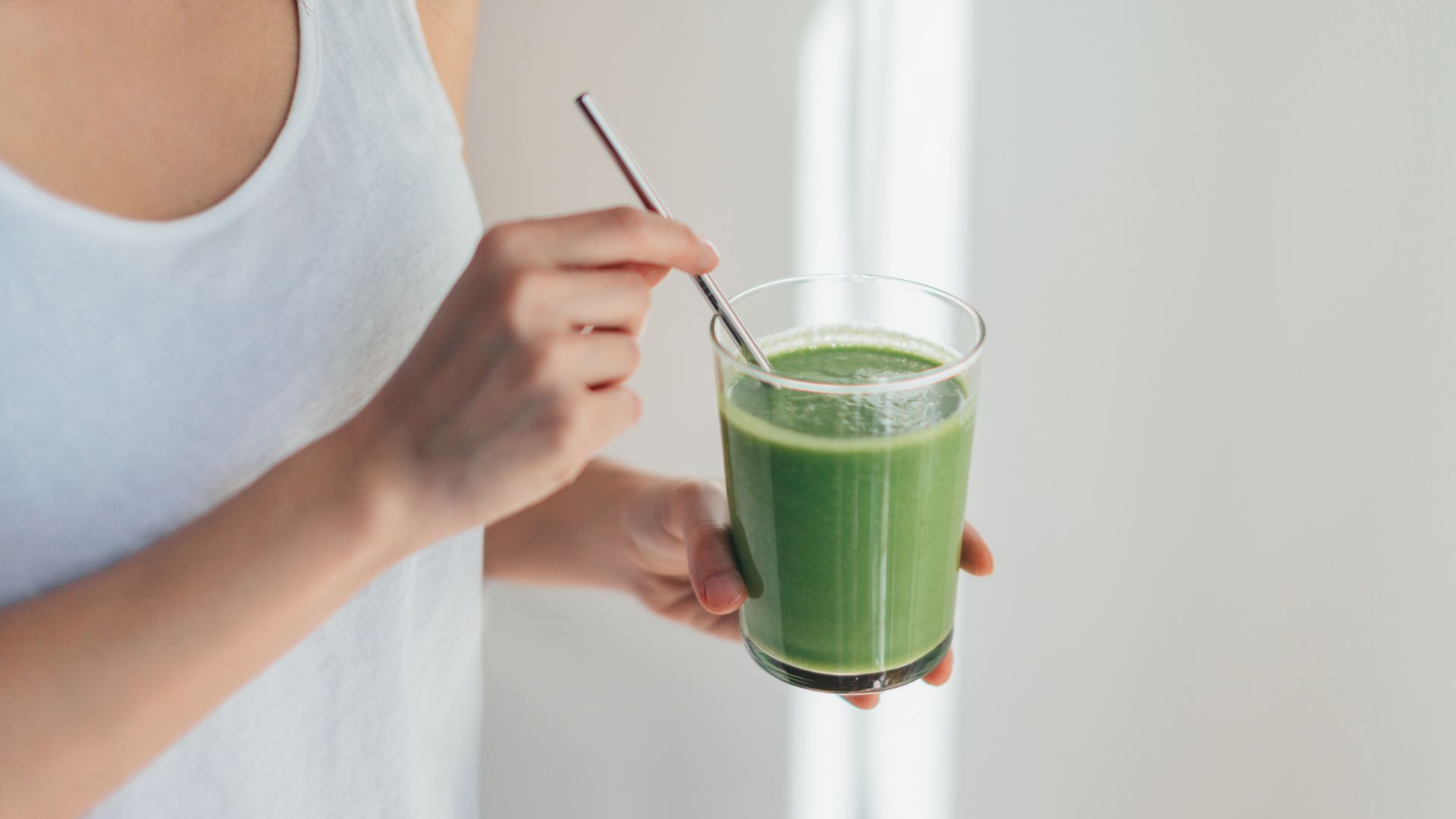 Cropped shot of young woman drinking vegan smoothie with metal straw.