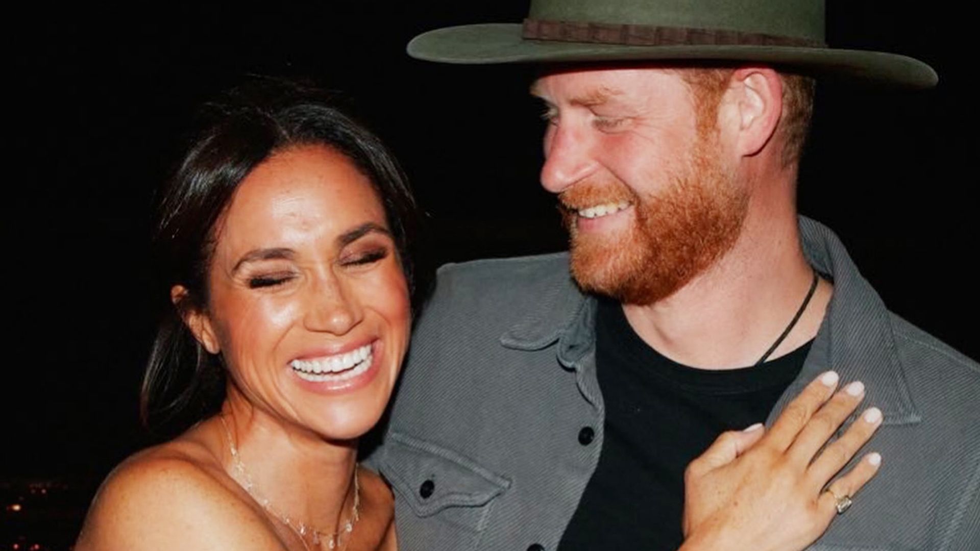 Harry wearing cowboy hat with arms around Meghan smiling in blue dress