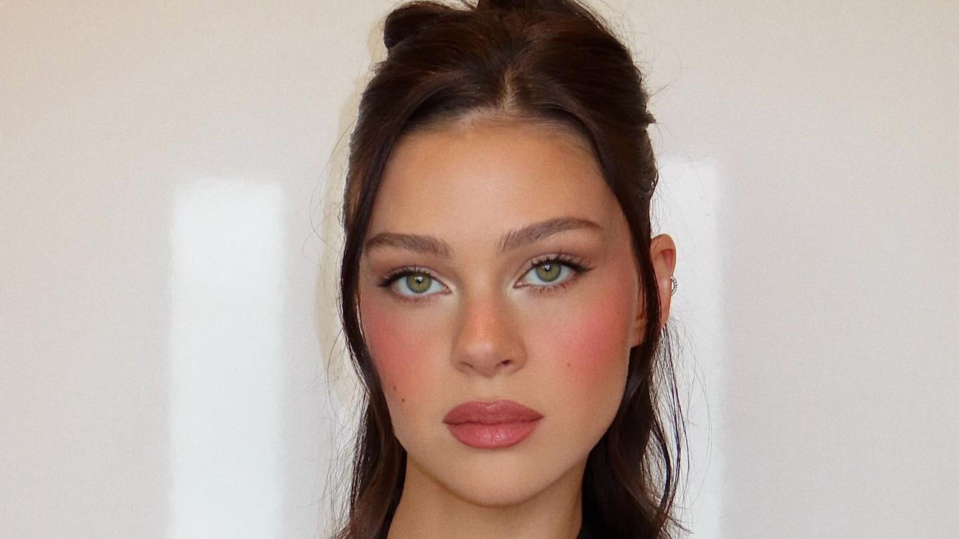 Nicola Peltz wearing a black halterneck top with her hair half-up half-down and a make up look featuring romantic rosy cheeks