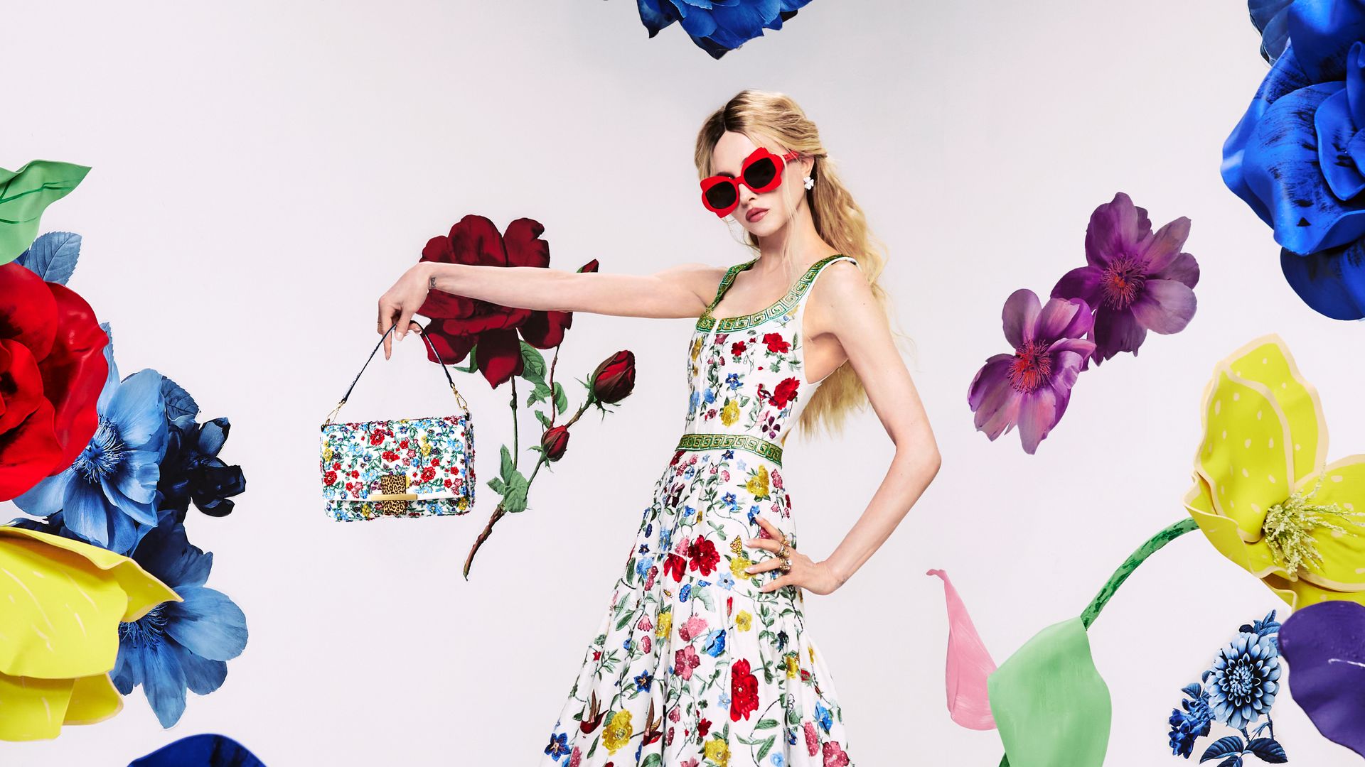 Alice + Olivia founder Stacey Bendet poses in a floral dress with a matching bag in a photostudio surrounded by flowers