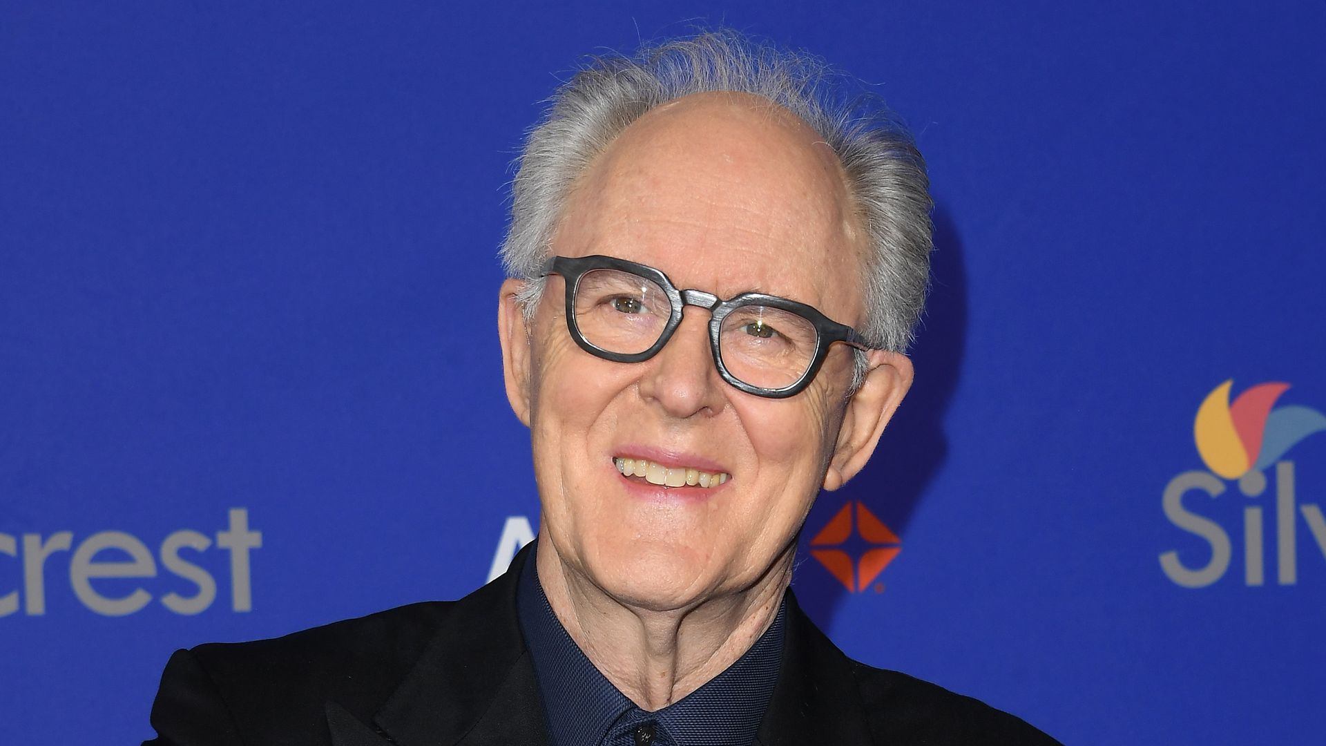 John Lithgow crossing his arms in a suit