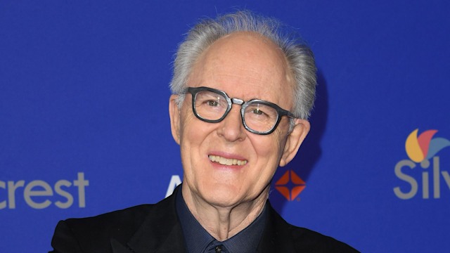 John Lithgow crossing his arms in a suit