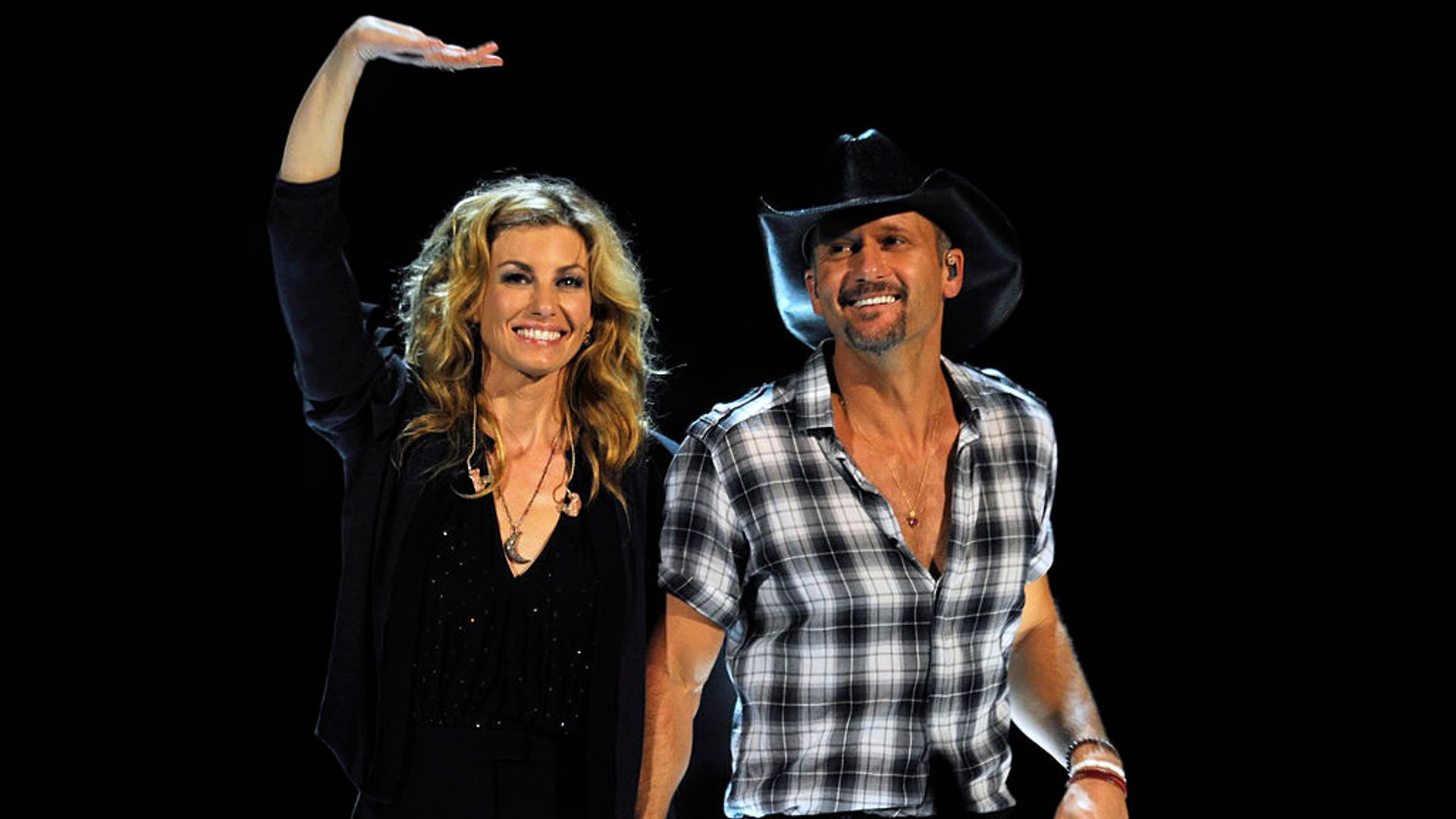 Faith Hill and Tim McGraw holding hands as they walk on stage. Faith waves at the crowd with her other hand. 