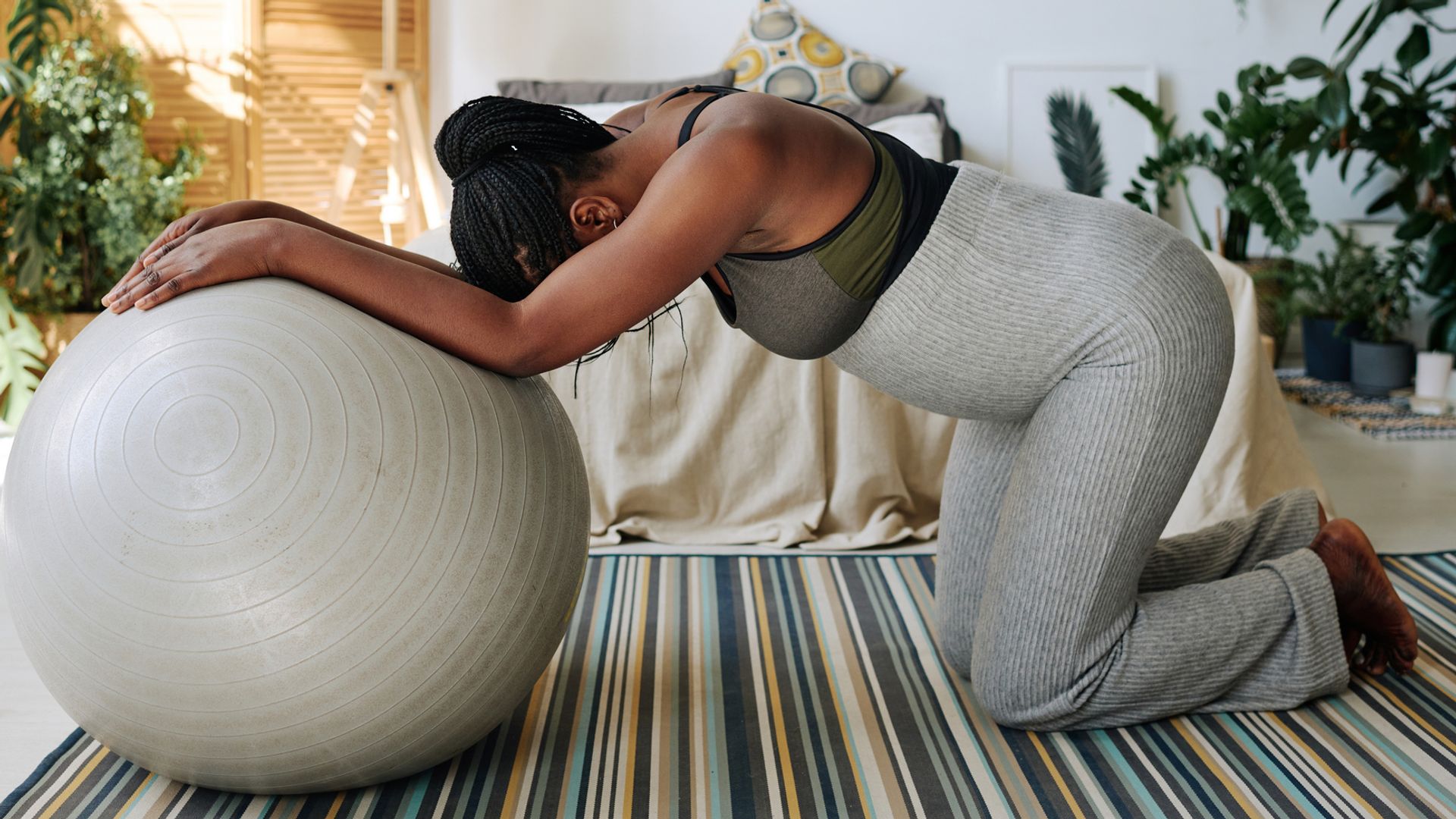 Pregnant woman leaning on fitness ball on a striped carpet