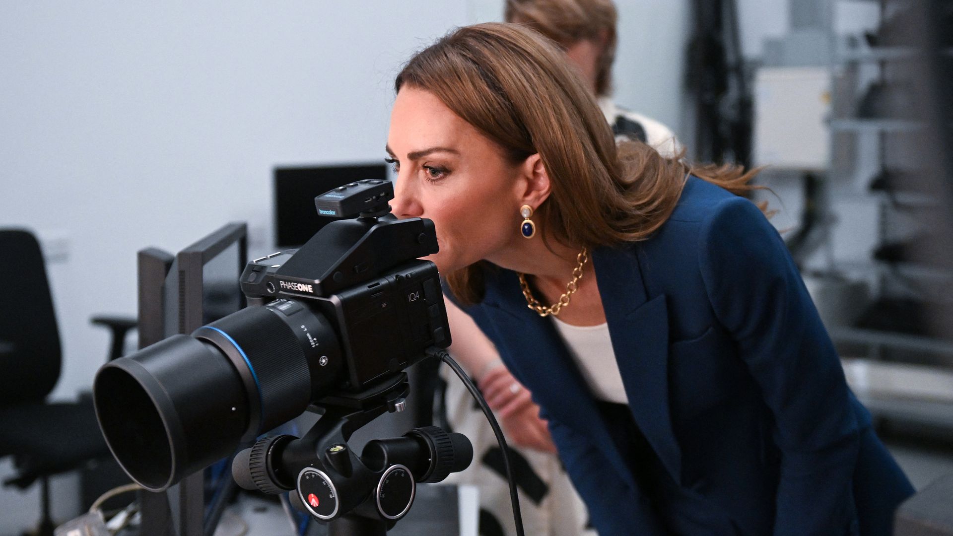 Kate Middleton in teal suit looking through viewfinder of a camera