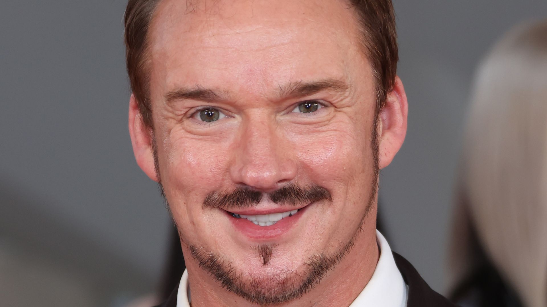 Russell Watson smiling in a black suit 